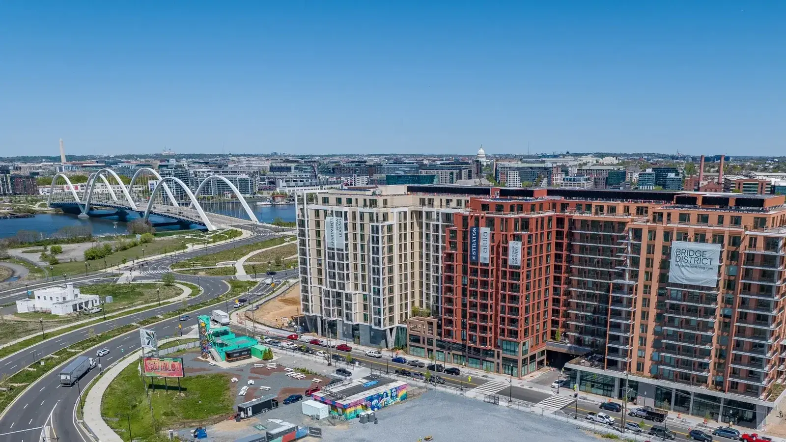 Aerial view of the Bridge District on the east bank of the Anacostia River, with the arches of the Frederick Douglass Memorial Bridge and the U.S. Capitol dome on the skyline beyond, Washington, D.C.