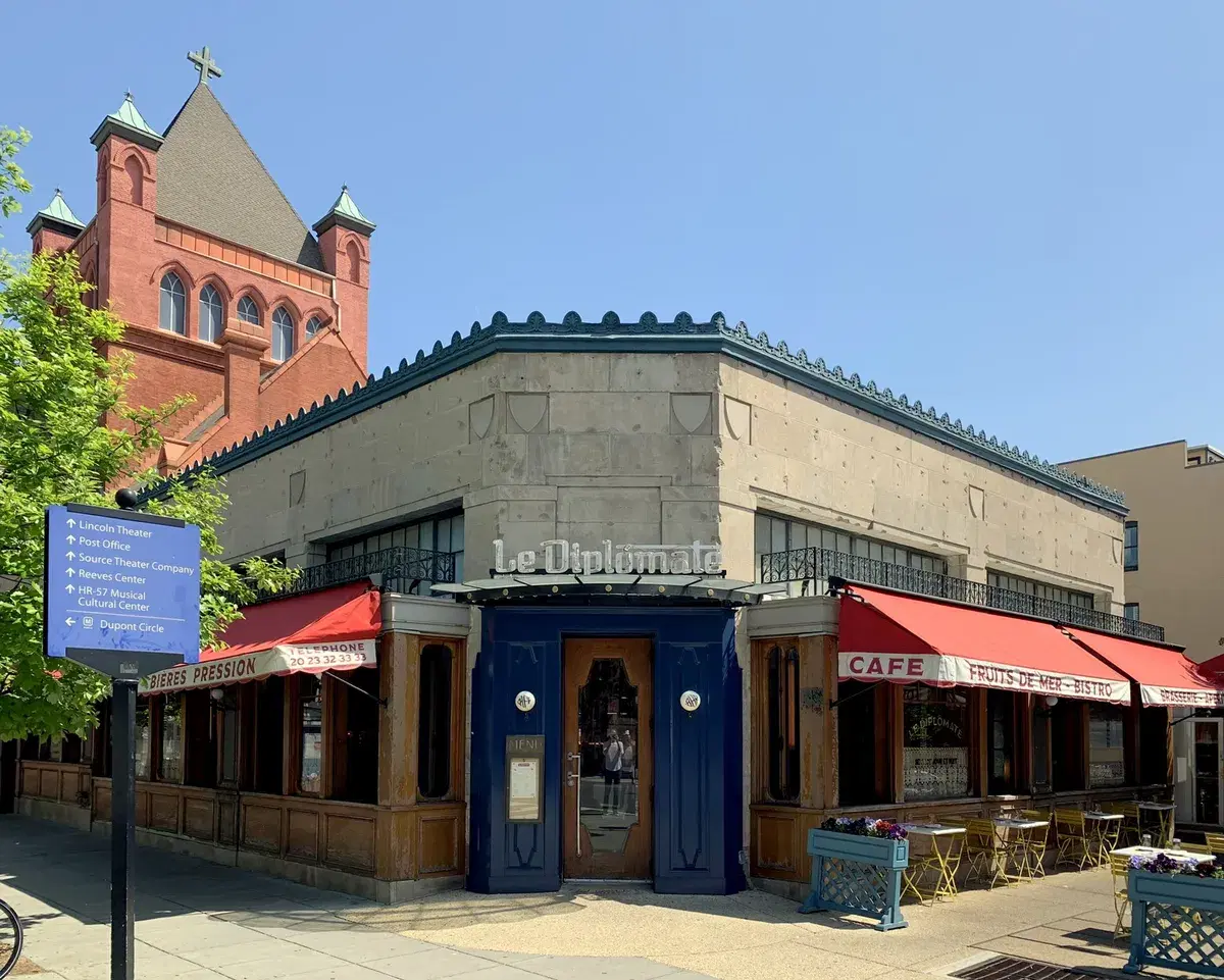 Le Diplomate's corner storefront at 14th and Q Streets NW, with red awnings, a blue door and a red-brick church tower behind, Washington, D.C.