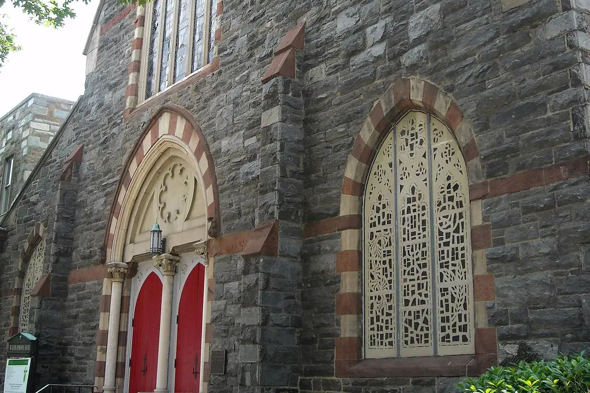 The gray stone front of St. Luke's Episcopal Church with red doors under a striped Gothic arch