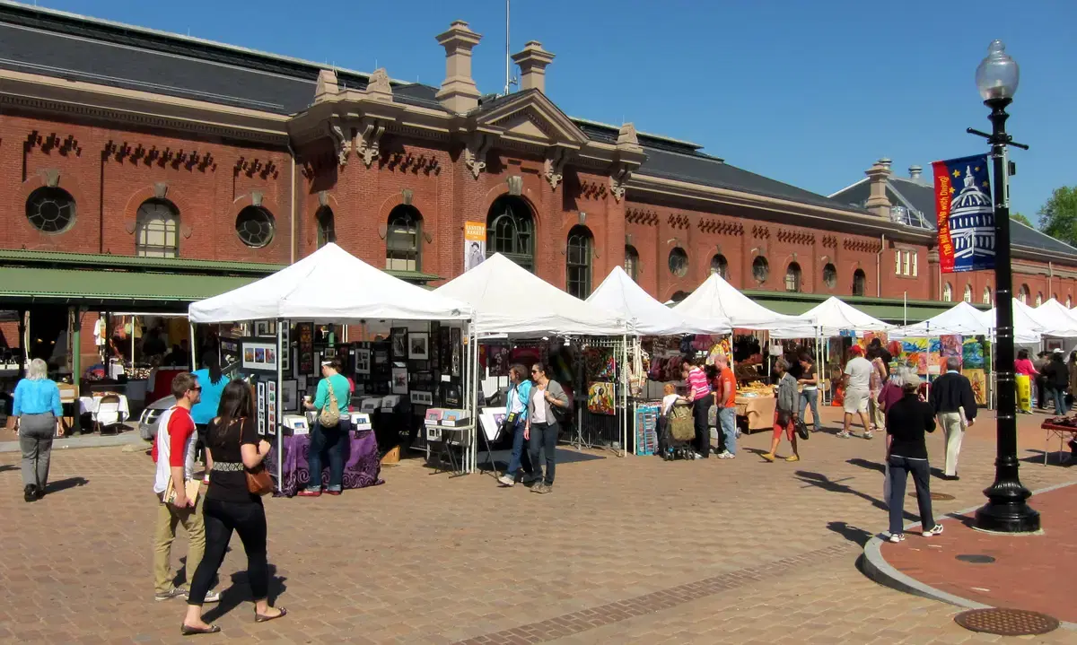 Vendor tents and shoppers along 7th Street SE in front of the red-brick 1873 Eastern Market hall, Washington, D.C.