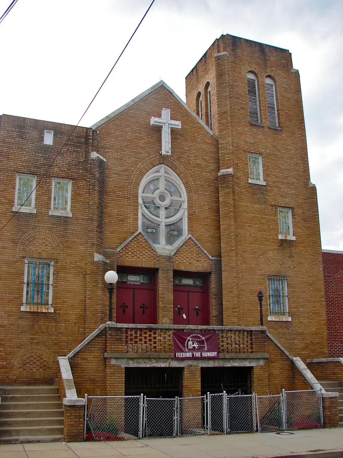 The tan brick bell tower, rose window and red doors of First Baptist Church of Deanwood