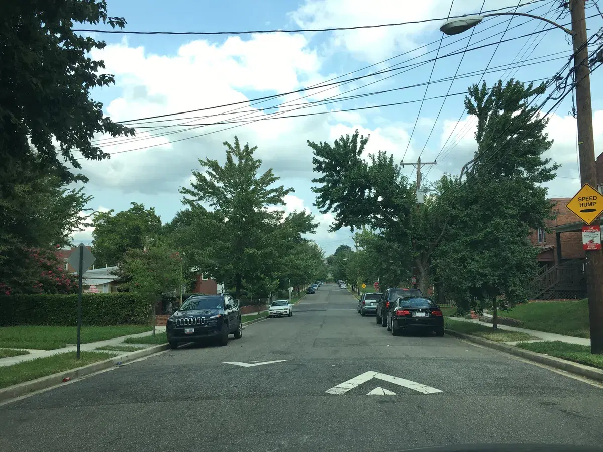 Cars parked along a tree-lined street of brick houses at Ames and 53rd Streets NE