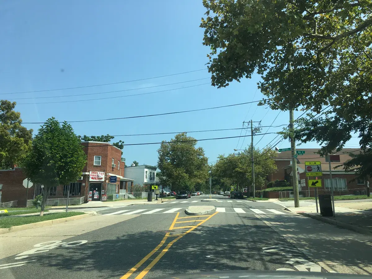 Sheriff Road NE at 46th Street, with a crosswalk, a brick corner store and street trees