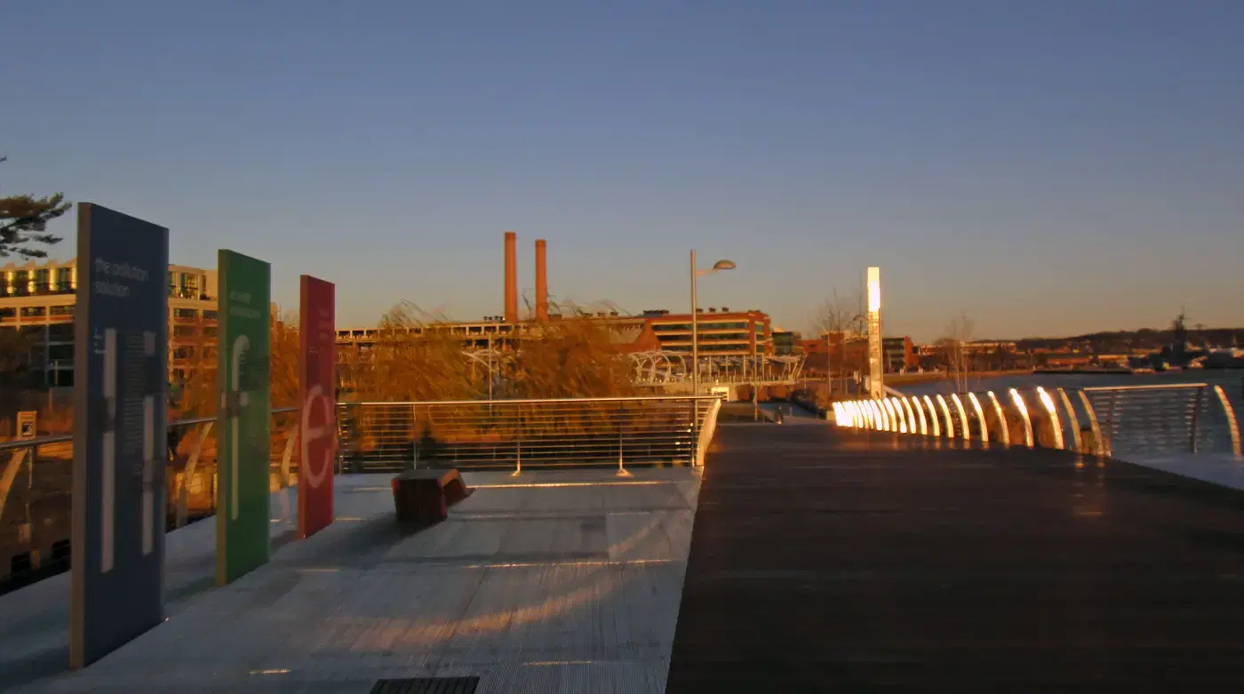 The riverwalk boardwalk at Diamond Teague Park at golden hour, with the old Navy Yard smokestacks beyond, Washington, D.C.