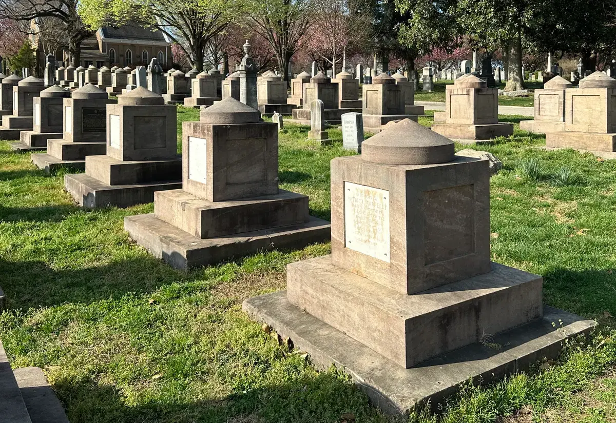 Rows of Latrobe cenotaphs on the green grounds of Congressional Cemetery, with the chapel and spring blossoms behind, Washington, D.C.