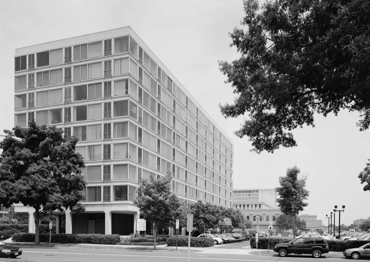 A nine-story modern apartment building with floor-to-ceiling windows, raised on columns above the street