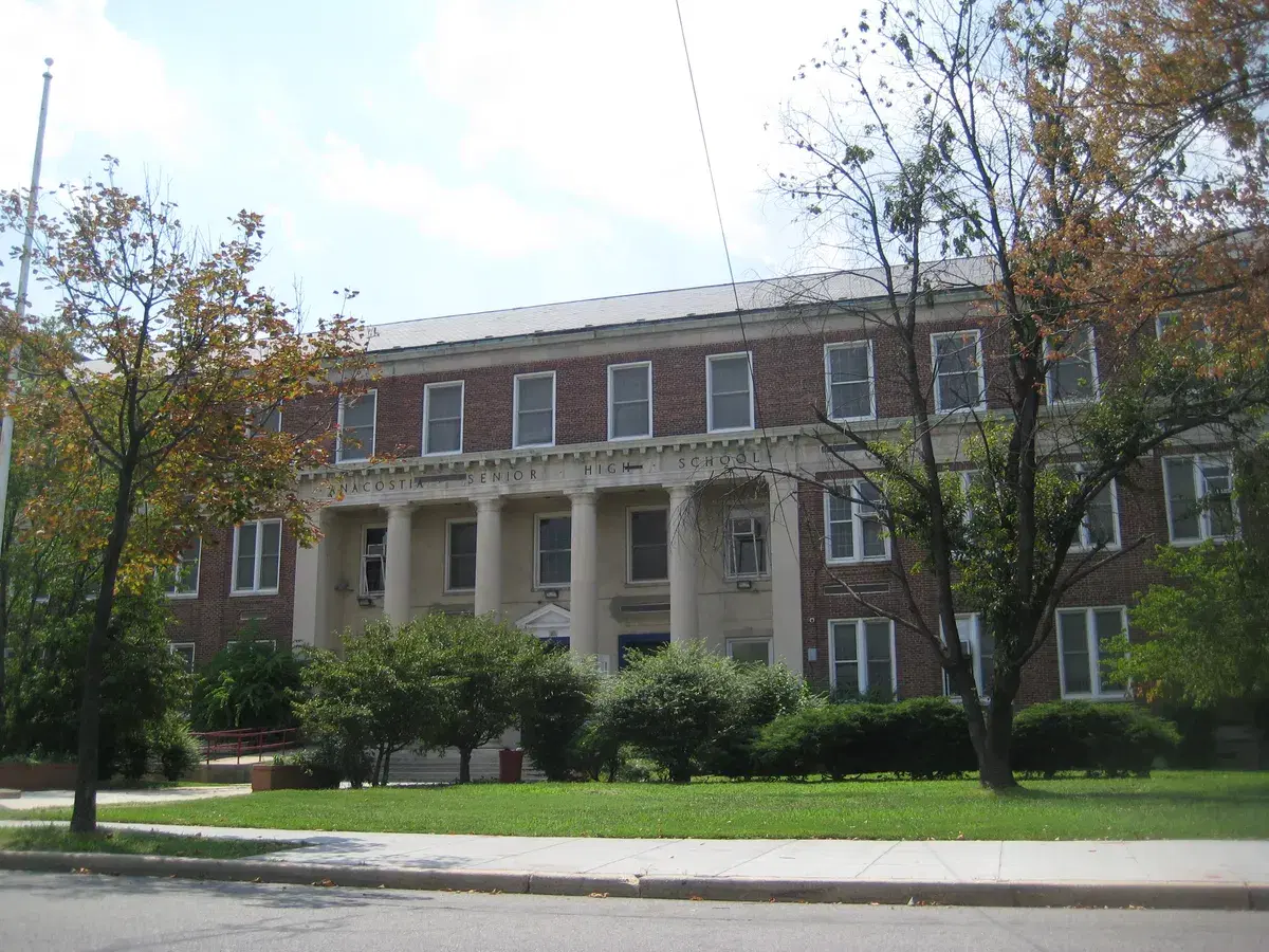 The columned brick facade of Anacostia High School behind a lawn and trees
