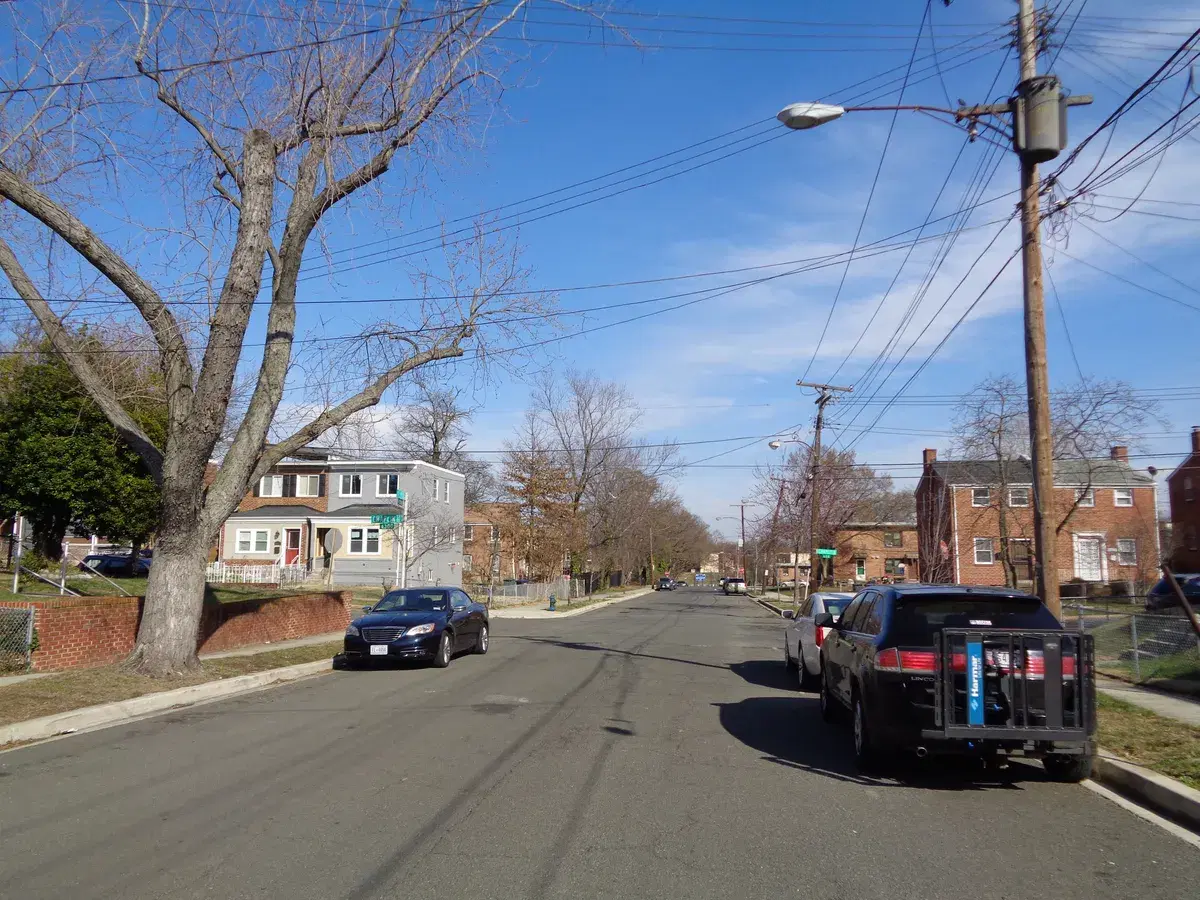 Cars parked along F Street SE at Chaplin Street in Benning Ridge, with brick houses and bare trees under a blue sky
