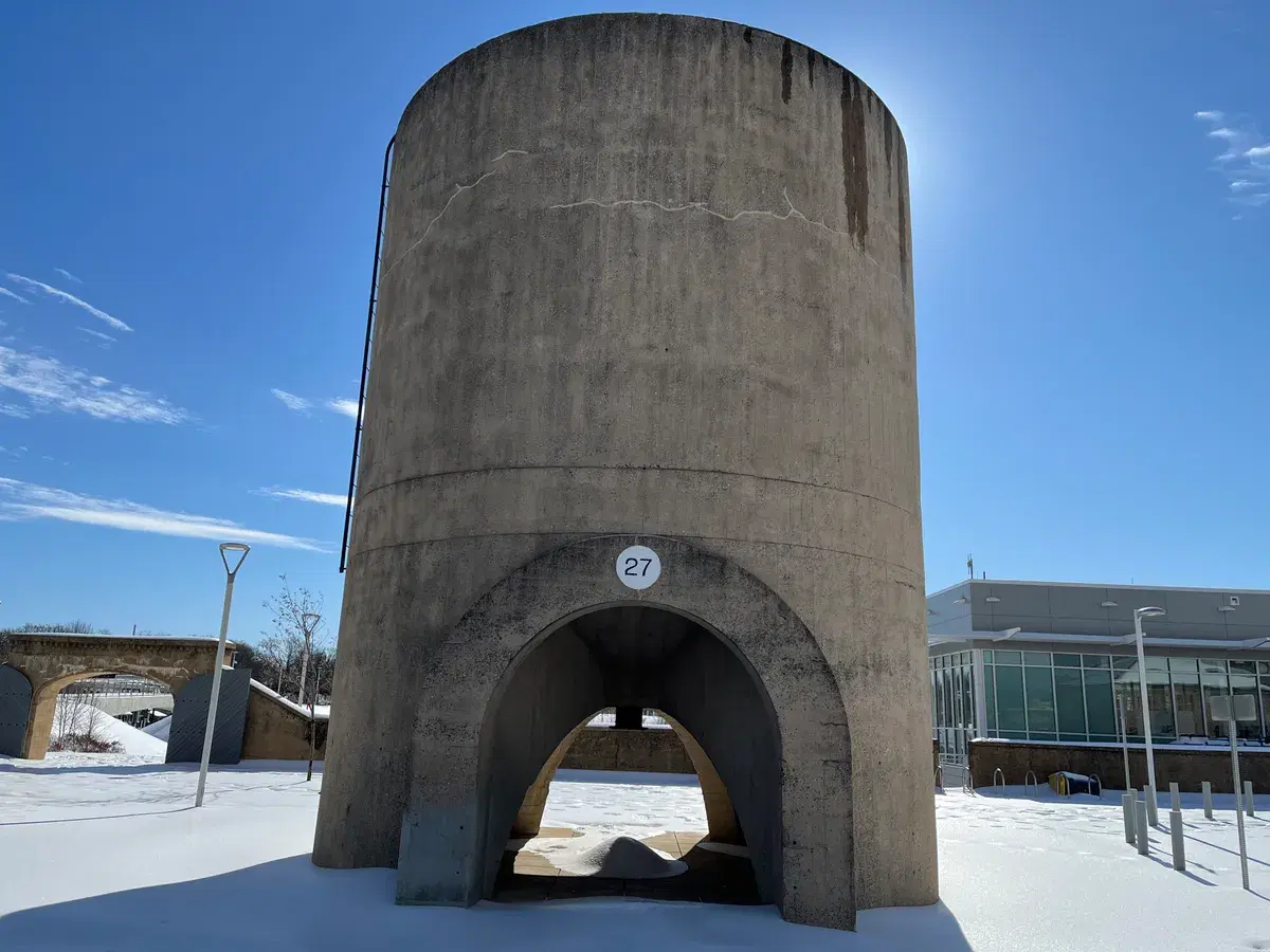 Sand bin 27 standing in the snow-covered plaza of Reservoir Park, with the recreation center behind it