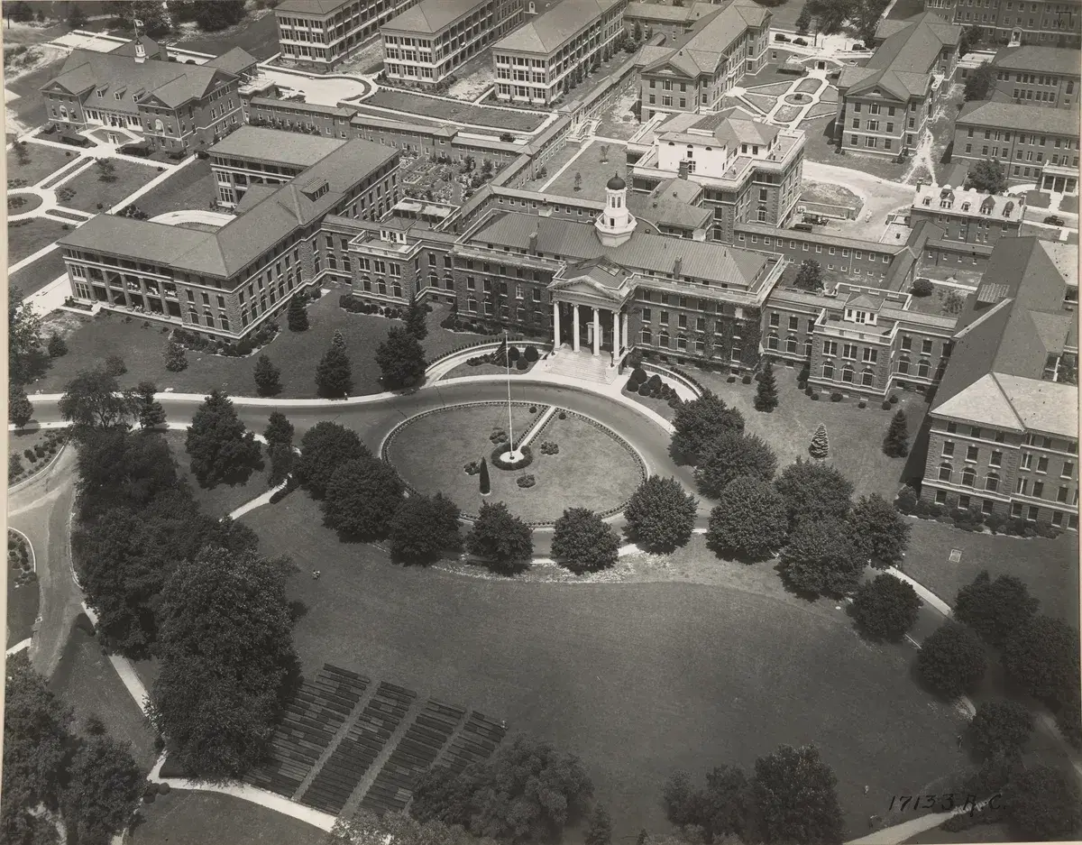 Aerial view of Building 1, its circular drive and flagpole, the lawn, and hospital wings behind