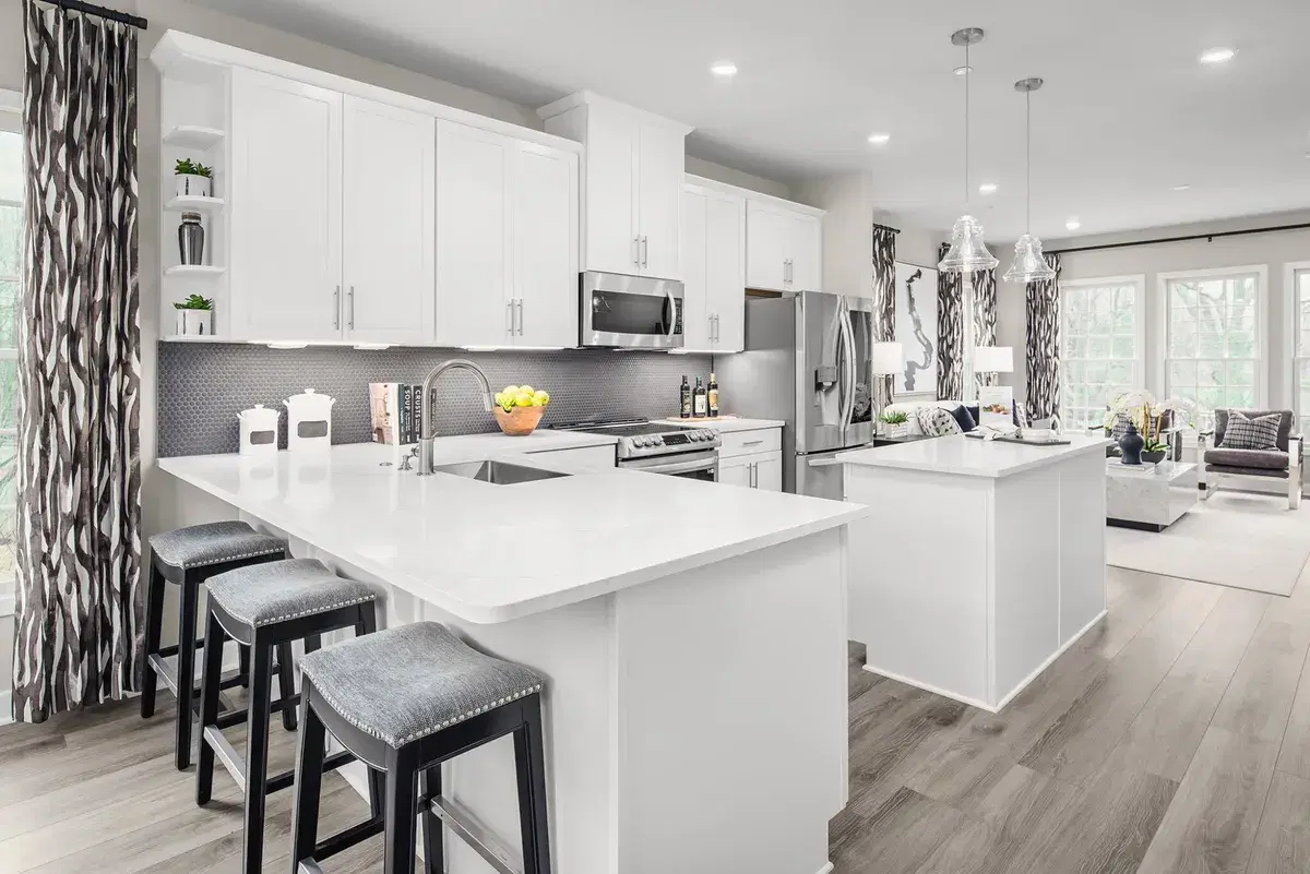 Kitchen with white cabinets, a quartz island and an open living room inside an Aspen Square townhome