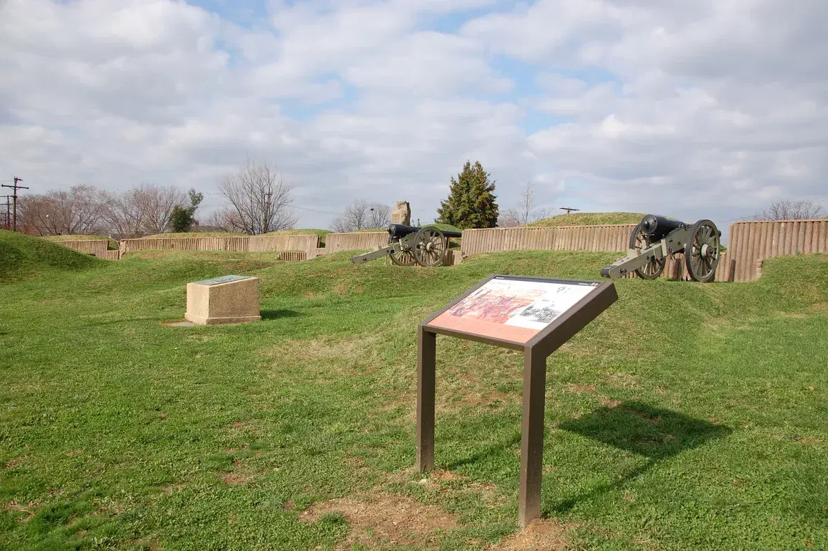 The restored earthworks of Fort Stevens with two cannons and a National Park Service sign