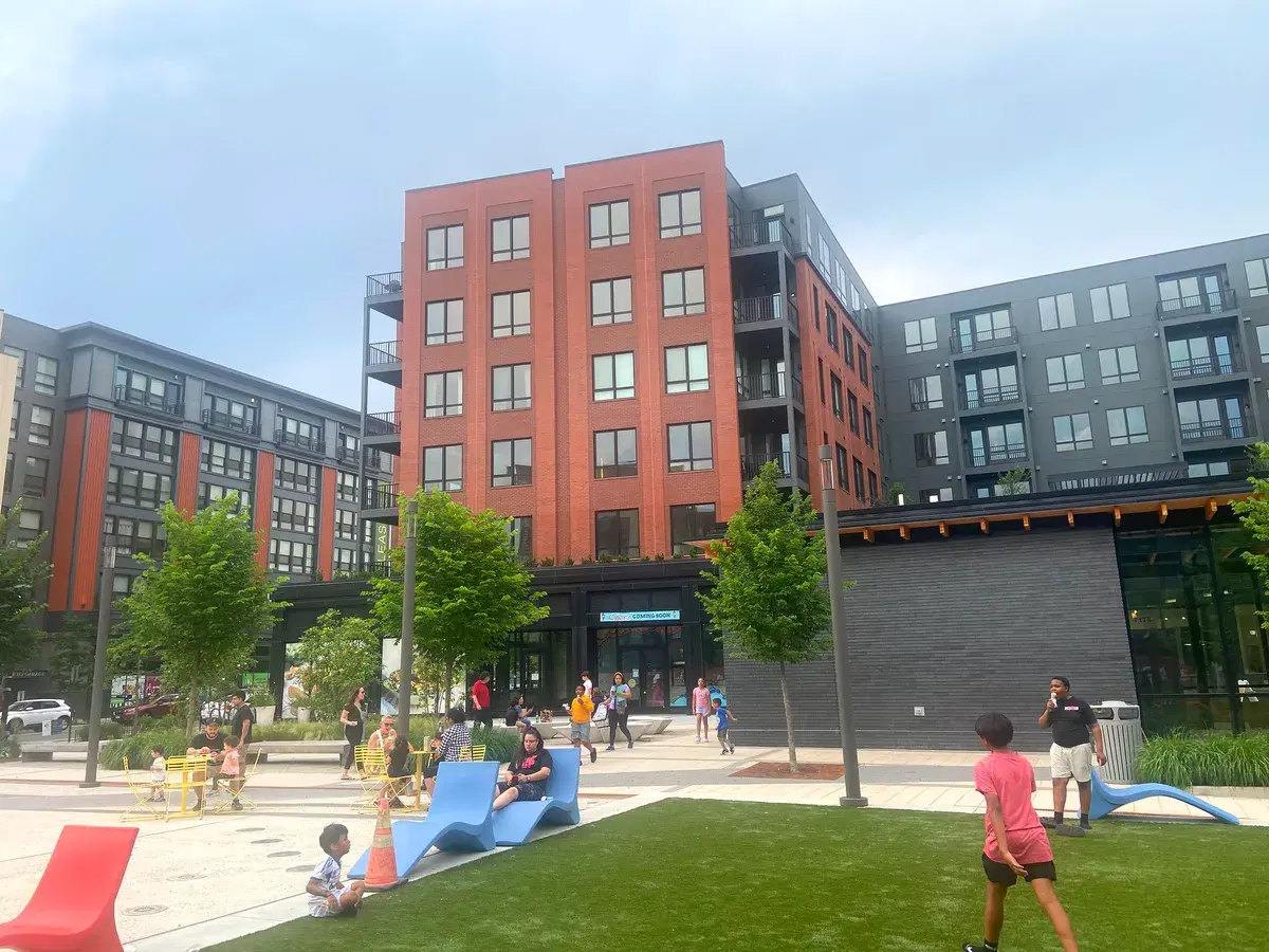 New apartment buildings around the plaza at the Parks at Walter Reed, with people on the lawn