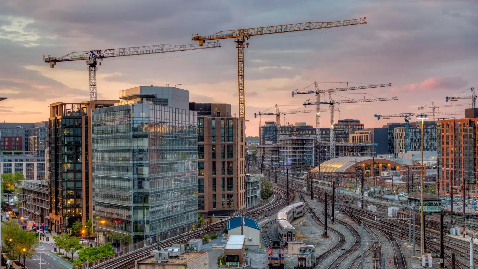 NoMa at sunset — glass and brick towers, construction cranes across the skyline, and the rail yard running past Union Station, Washington, D.C.