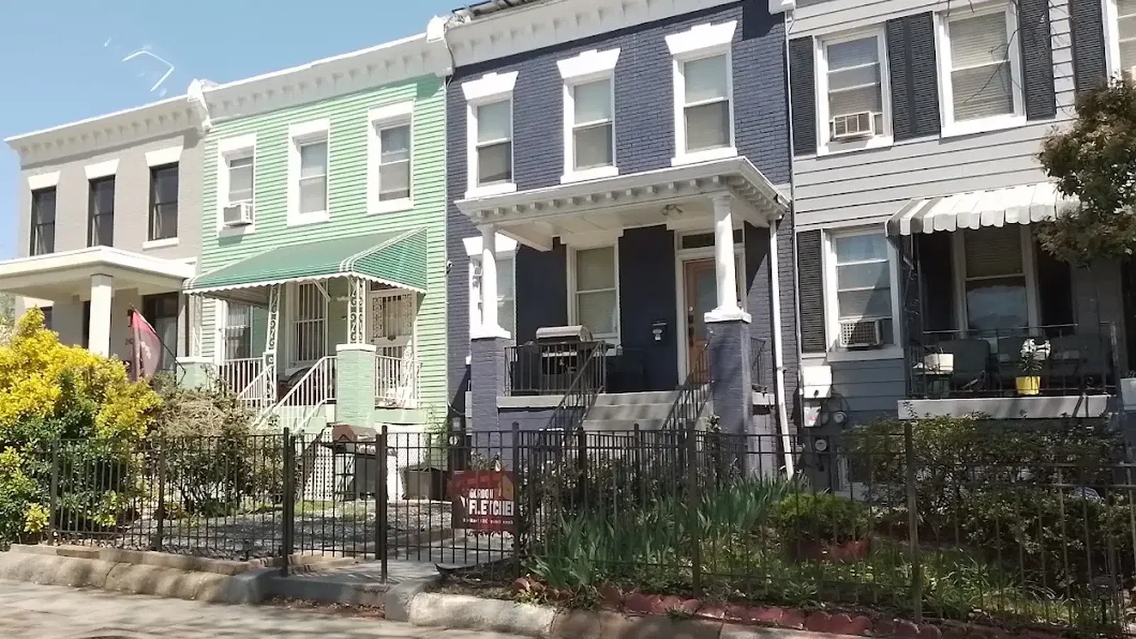 A row of Petworth rowhouses in Washington, D.C. — grey, mint green, navy and pale grey fronts with columned porches, iron fences and front gardens in early spring.
