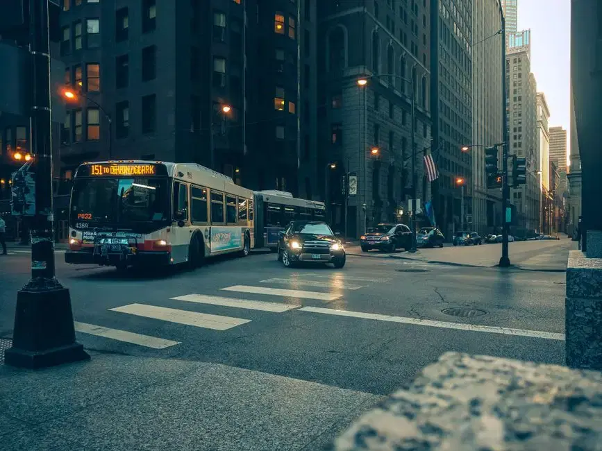 US city bus crossing a downtown intersection at twilight, American flag visible