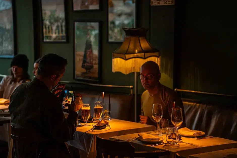 Warm dimly lit restaurant interior, diners at candlelit tables under a fringed lamp