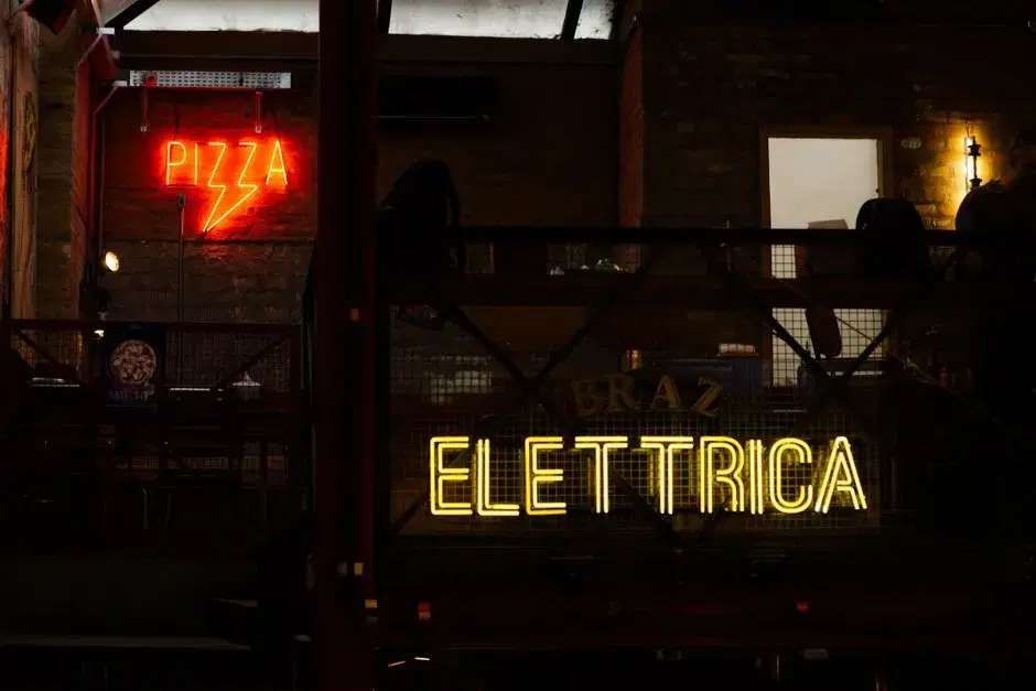 Red PIZZA neon and yellow neon signage in a moody industrial pizza bar at night