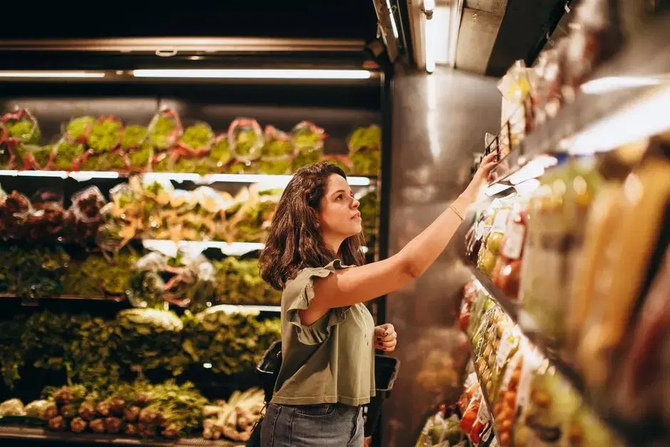 Shopper reaching for produce in a warmly lit grocery produce aisle, face in profile