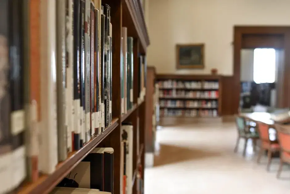 Wooden library bookshelves in the foreground with a warm reading room beyond