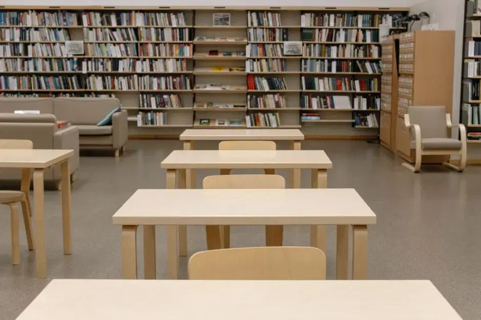 Bright library reading room with wall of bookshelves, light-wood study tables and lounge seating