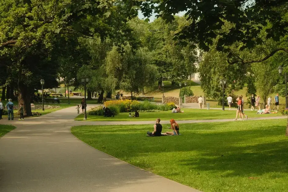 Leafy city park with winding path, flower beds, and people relaxing on the lawn