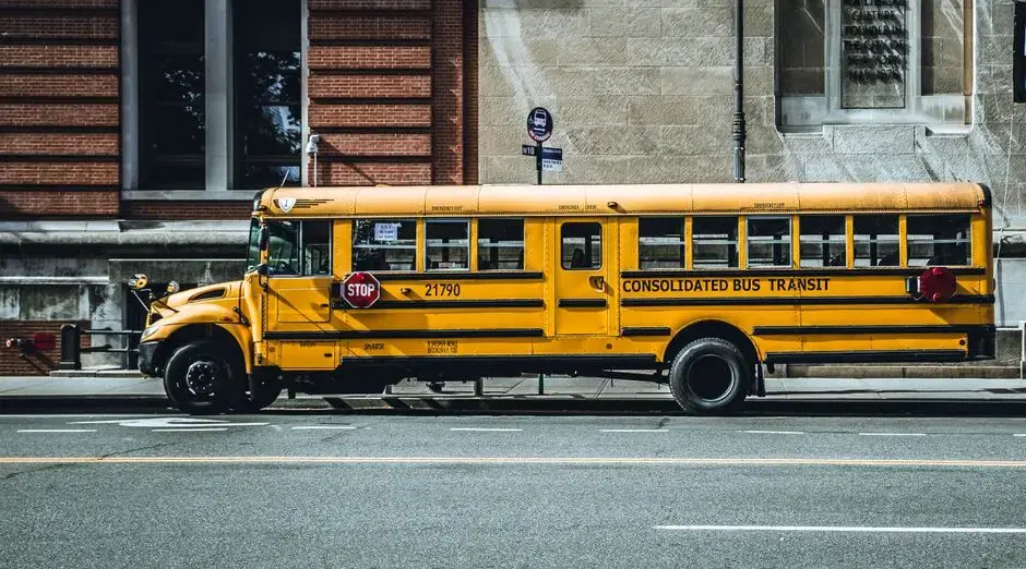 Classic yellow school bus in side profile against brick and stone city buildings