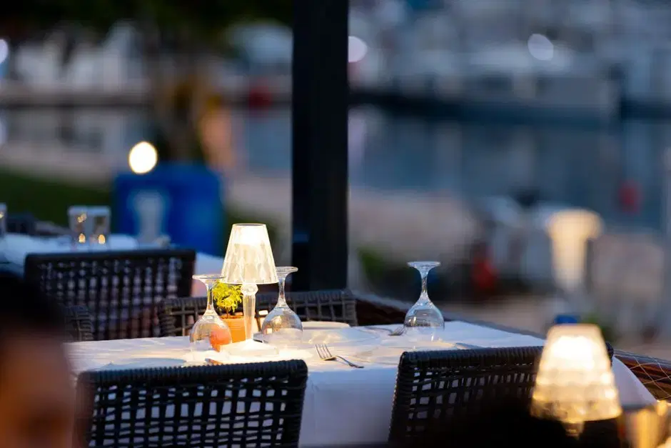 Candlelit outdoor dinner table at a marina at twilight — generic dockside-dining vibe (card is about the dining scene, no venue depicted)