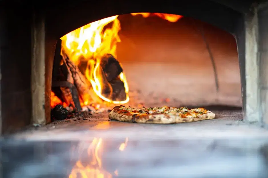 Artisan pizza baking in a flaming wood-fired brick oven — food ambience echoing the card's Timber Pizza anchor, no venue claim