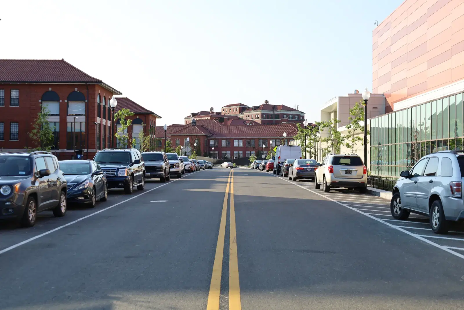 A campus street on St. Elizabeths East, Washington, D.C. — red-brick hospital buildings with tile roofs along new sidewalks, street lamps and young trees, the arena at right.