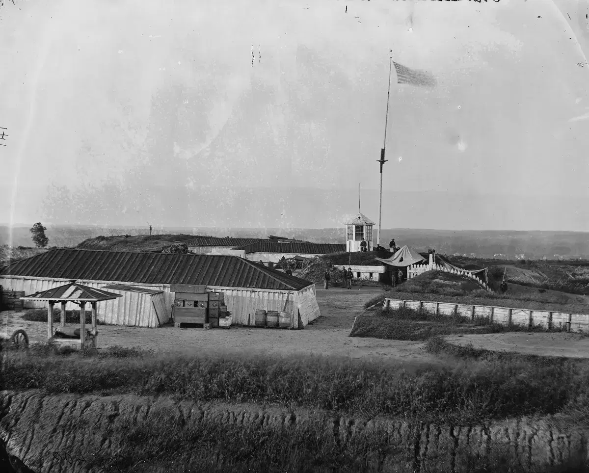 Inside Fort Lincoln: low wooden buildings, earth walls and a flag on a tall pole, with open country beyond