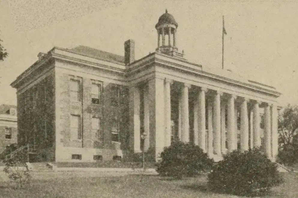 A two-story stone building with a row of tall columns across the front and a small domed cupola on the roof