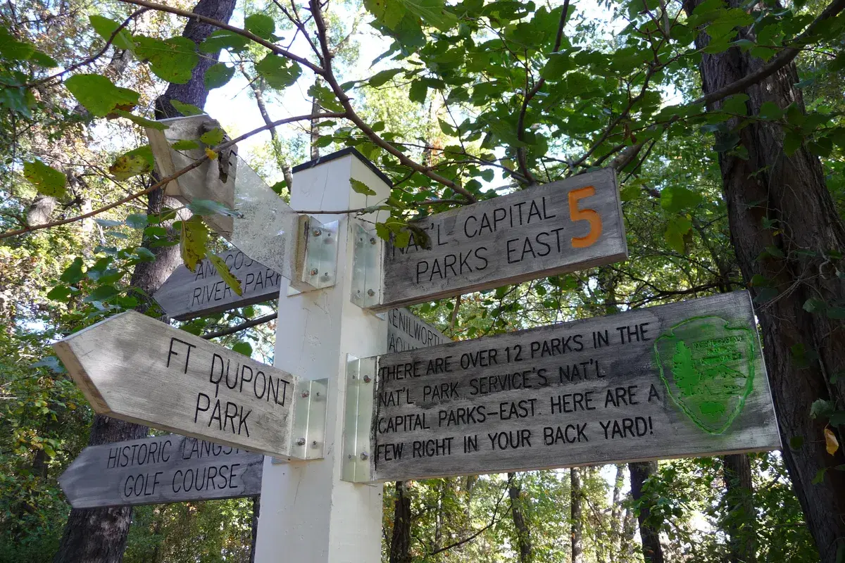 A wooden trail signpost in the woods pointing to Fort Dupont Park and historic Langston Golf Course