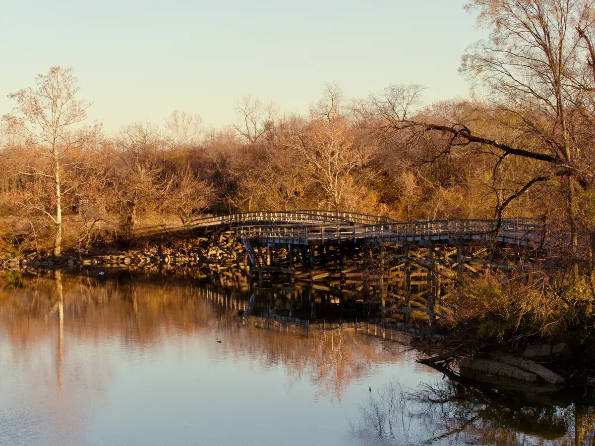 The wooden footbridge between Heritage Island and Kingman Island, reflected in still water at sunset