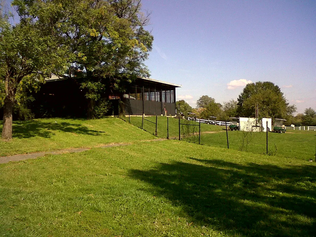 The Langston Golf Course clubhouse on a grassy rise, with golf carts parked by the fence