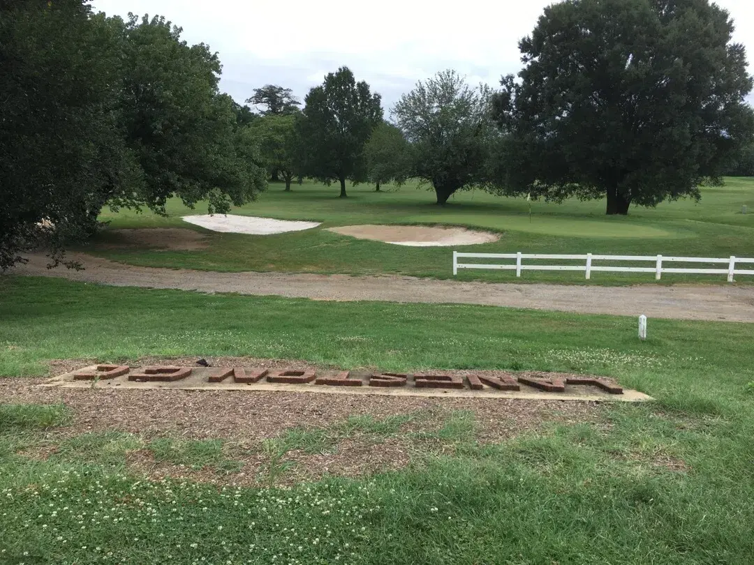The brick LANGSTON GC letters set in the grass beside a green and bunkers at Langston Golf Course