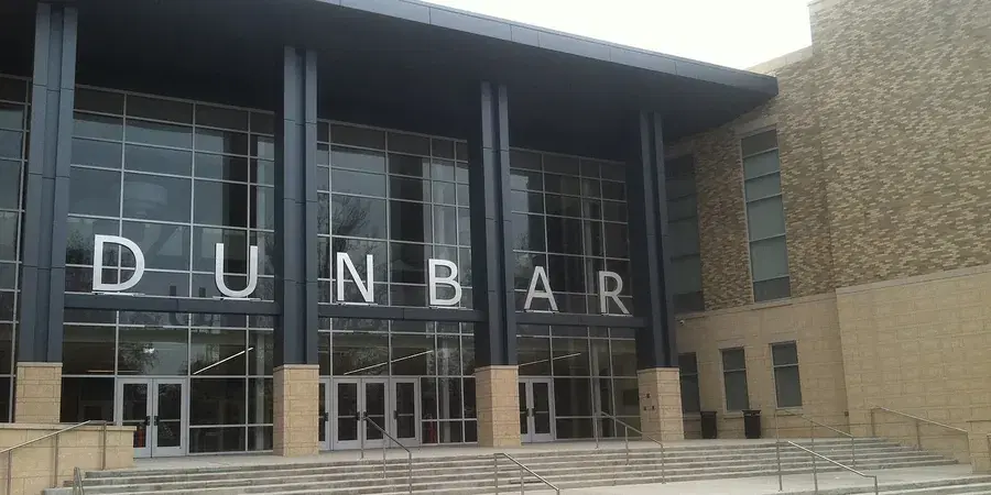 The glass entrance of the rebuilt Dunbar High School campus, its name in tall letters across the facade, Washington, D.C.