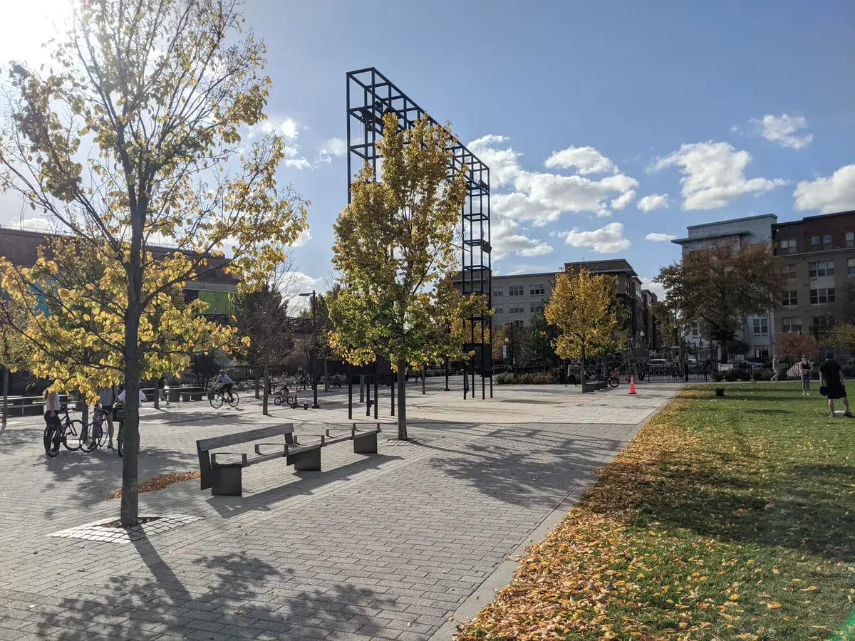 Paved plaza, benches and trees in fall color at Alethia Tanner Park, with a lawn on the right