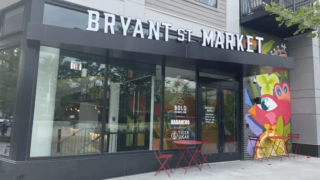 The Bryant St Market storefront, with red cafe tables outside and a colorful mural beside the door