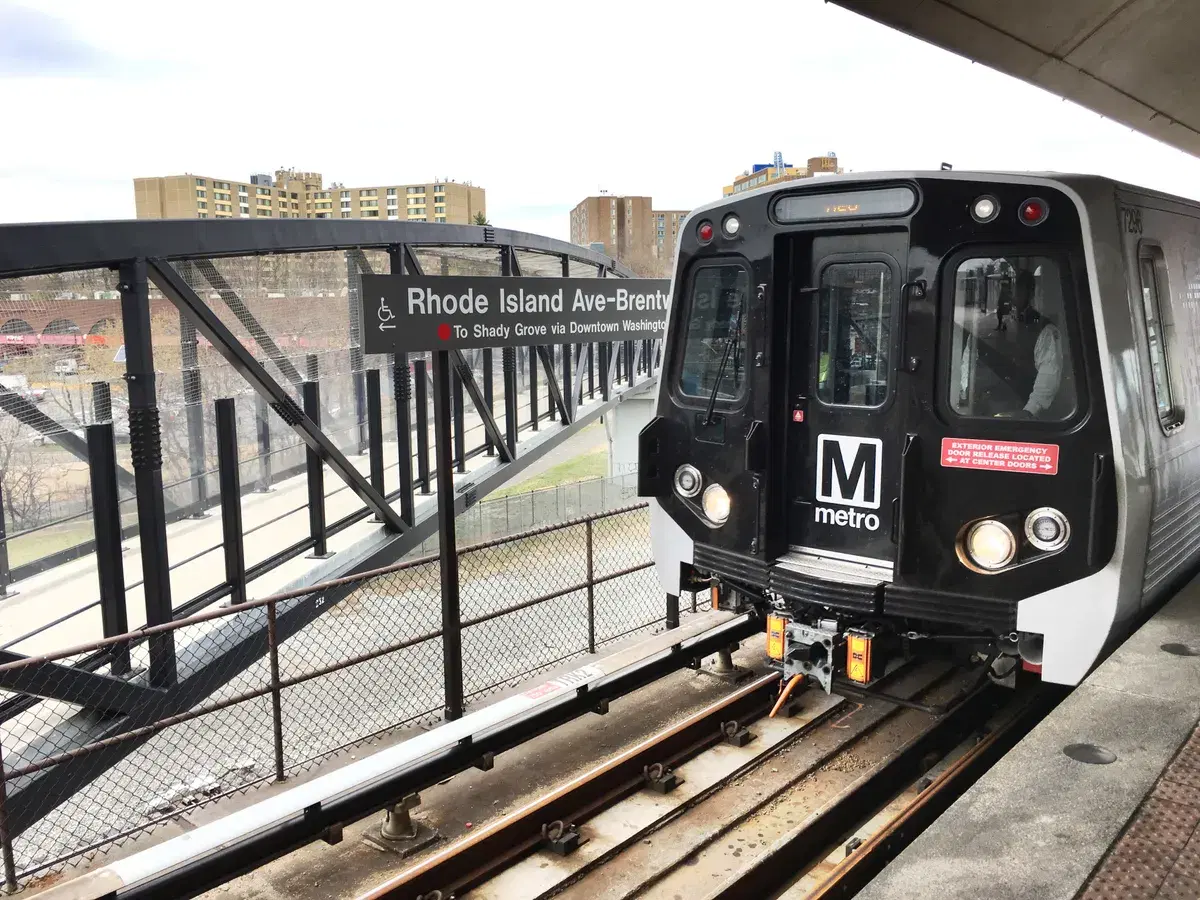 A Red Line train at the Rhode Island Ave–Brentwood platform beside the station sign and footbridge