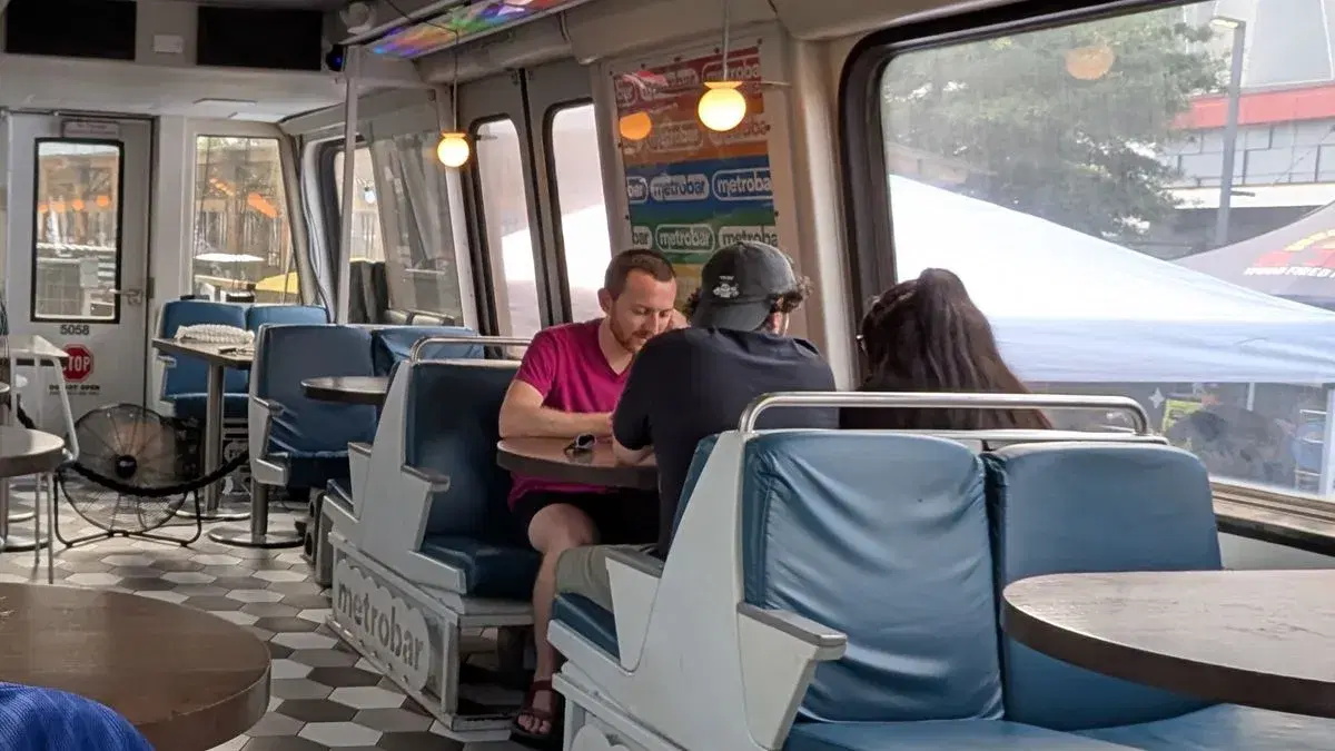 Inside Metrobar's railcar, with blue Metro seats lettered metrobar and customers at a table