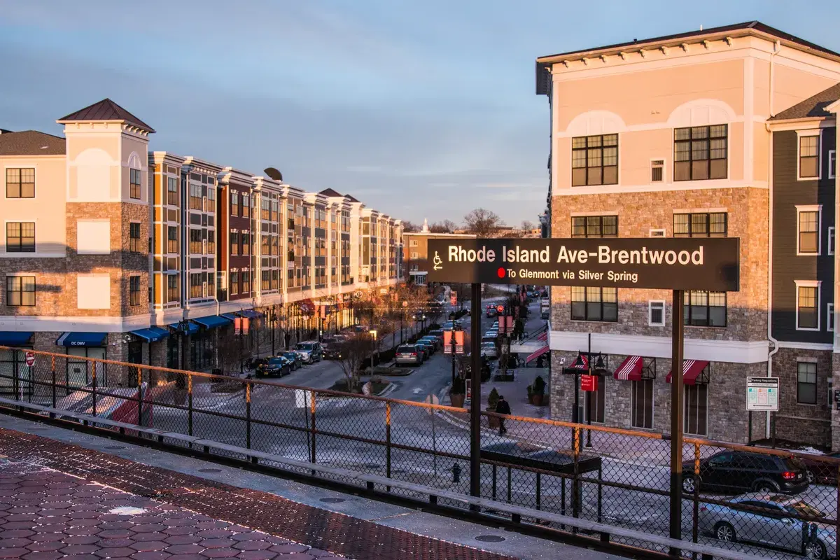 The Rhode Island Ave–Brentwood station sign on the platform, with apartment buildings and shops below at sunset