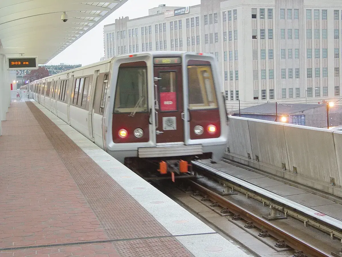 A Red Line train at the platform of the new station, with a large white warehouse building behind