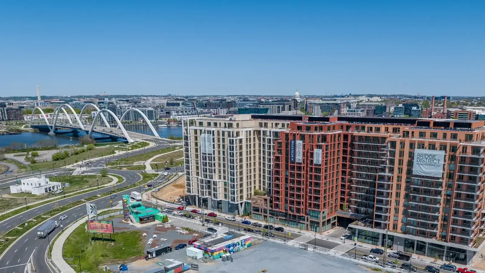 Aerial view of the Bridge District on the east bank of the Anacostia River, with the arches of the Frederick Douglass Memorial Bridge and the U.S. Capitol dome on the skyline beyond, Washington, D.C.