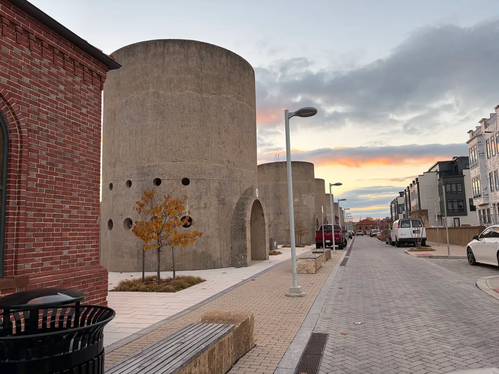 Concrete sand bins line a new brick street at sunset in the Reservoir District, with townhomes at right, Washington, D.C.